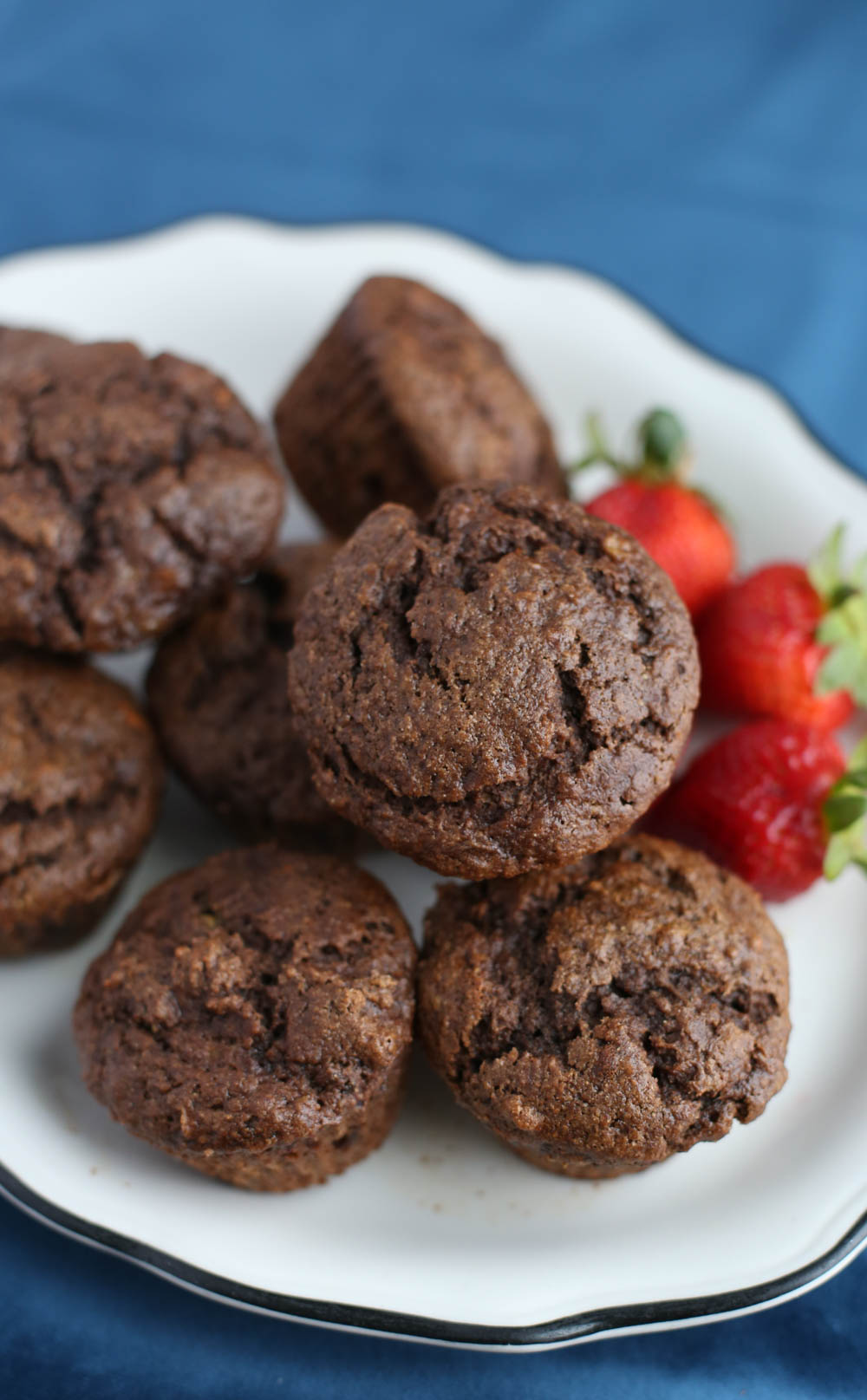 Chocolate banana muffins stacked on a white plate with a few whole strawberries on one side.