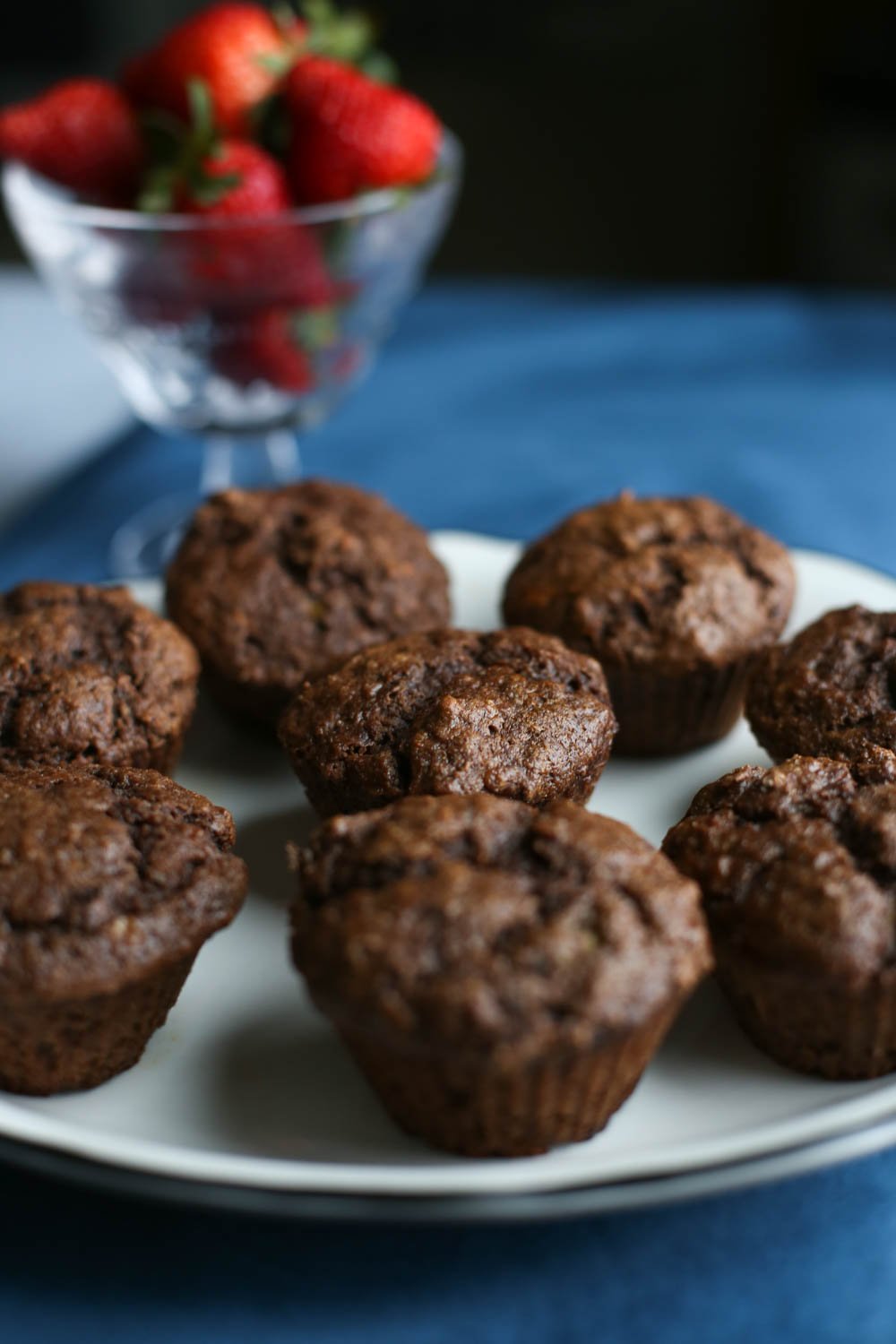 Chocolate banana muffins on a white plate with a bowl of whole strawberries in the background.