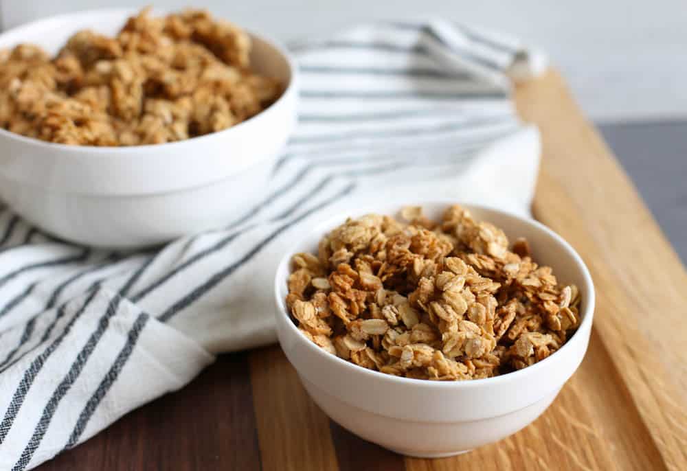 Homemade granola in white bowls o a wooden cutting board.