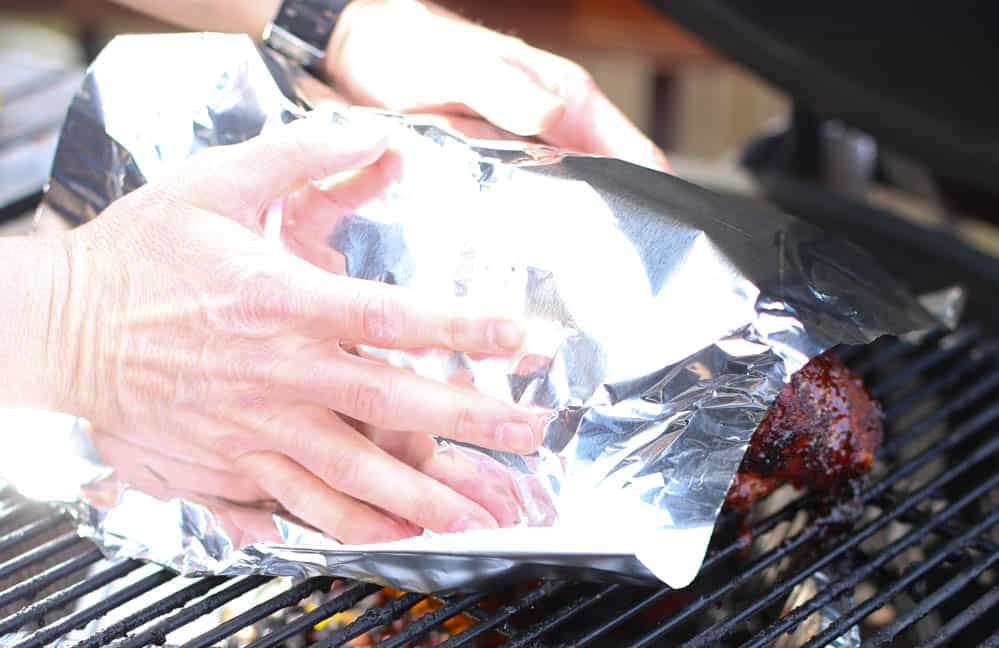 Smoked pork shoulder on the grill of a smoker with foil being tented over it.