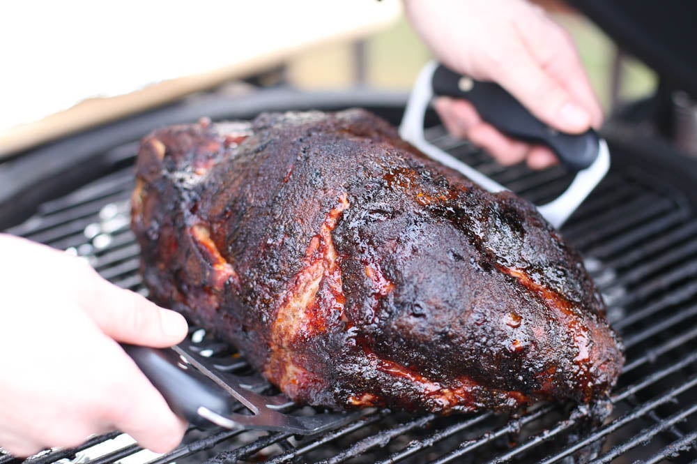 A smoked pork shoulder being removed from the smoker with meat shredders.