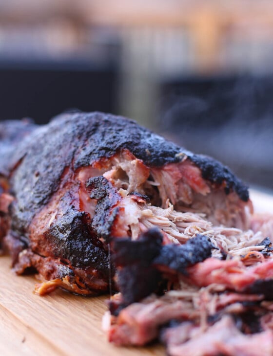 A fully smoked pork shoulder on a wooden cutting board, partially shredded.