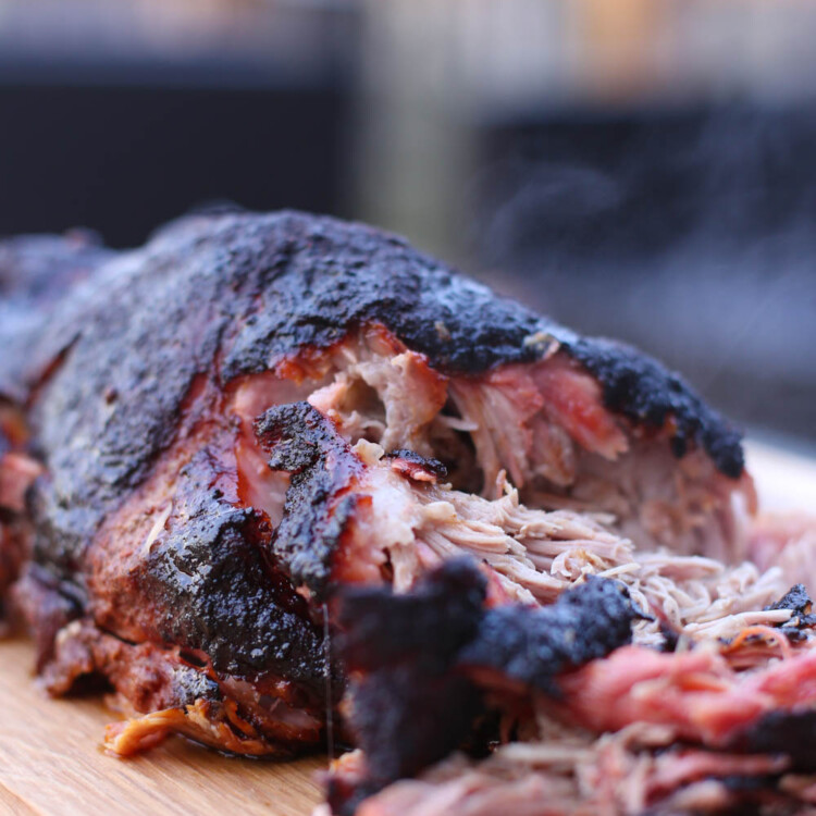 A fully smoked pork shoulder on a wooden cutting board, partially shredded.
