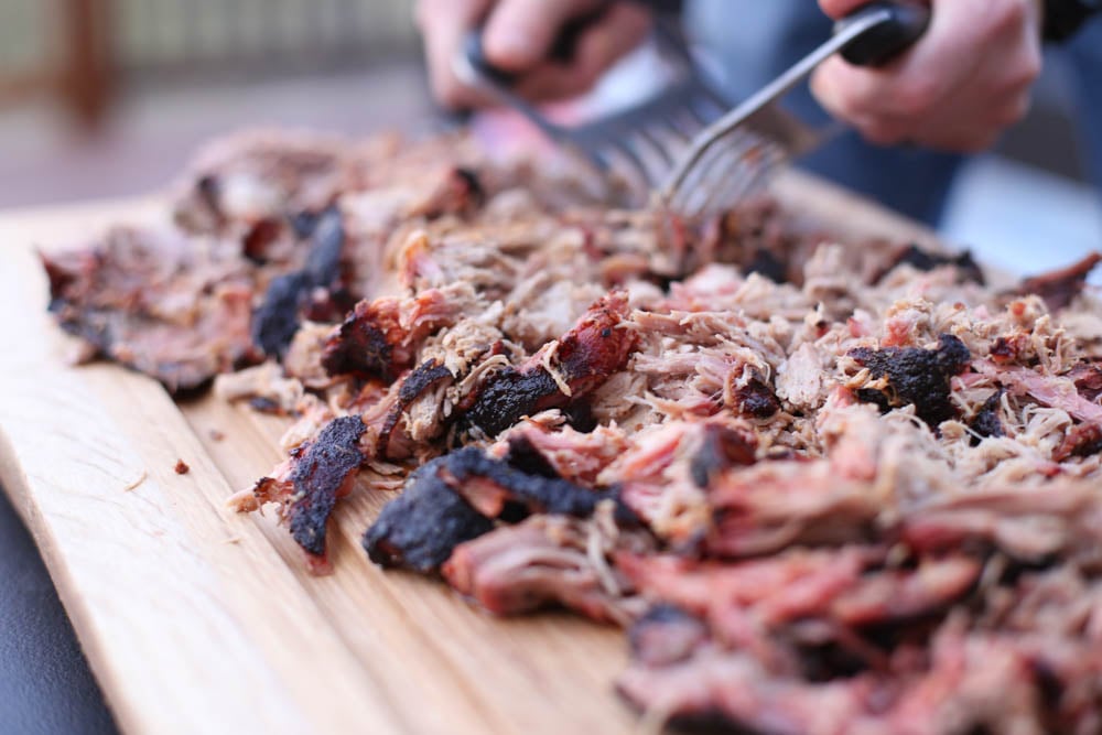 Smoked pulled pork on a cutting board with meat shredders finishing the shredding.