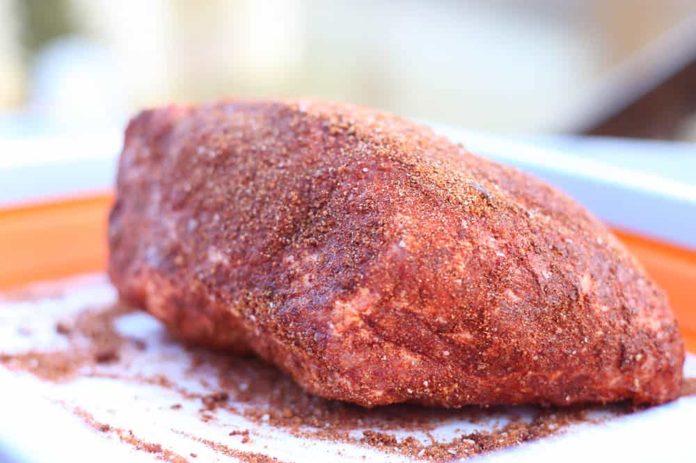 An uncooked pork shoulder with seasoned rub all over it.