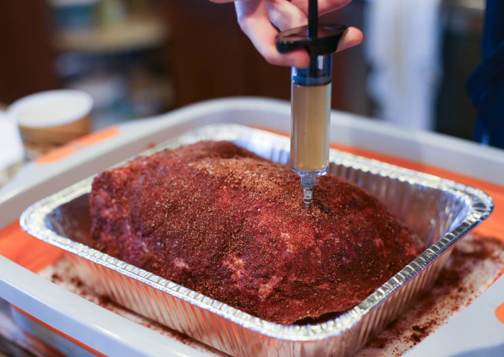 A pork butt with a rub on it getting a juice injection.