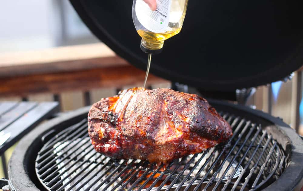 Agave being drizzled over a partially cooked pork shoulder on the grill of a smoker.