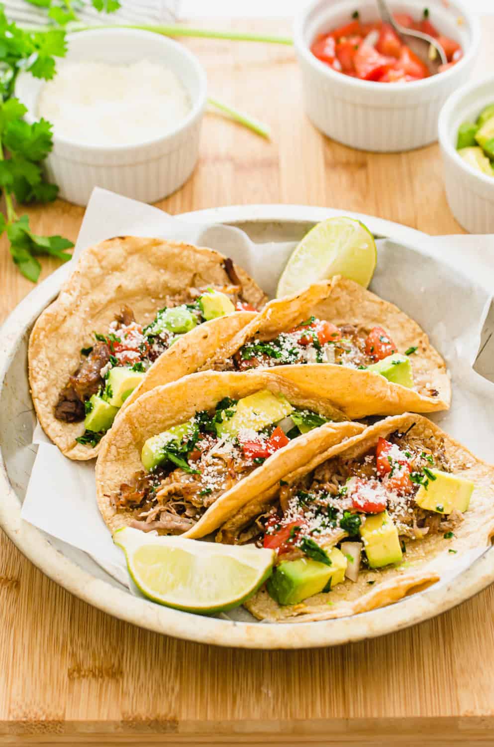 A plate of carnitas tacos with toppings in the background.