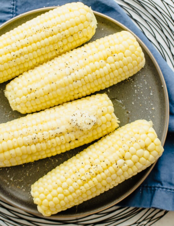Four ears of corn on the cob on a plate with a pat of butter on top.