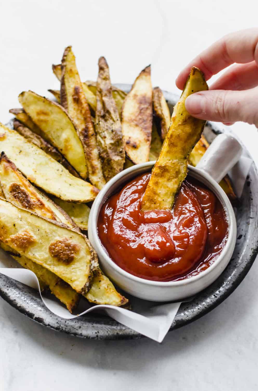 A hand dipping an oven steak fry into ketchup.