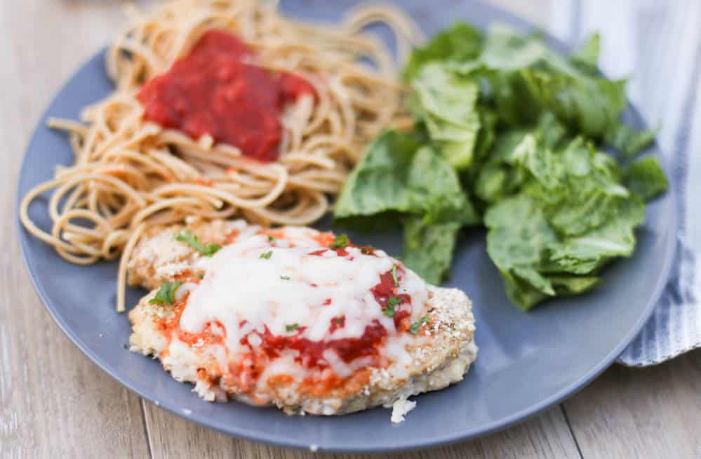 Chicken parmesan on a plate with pasta and a salad 