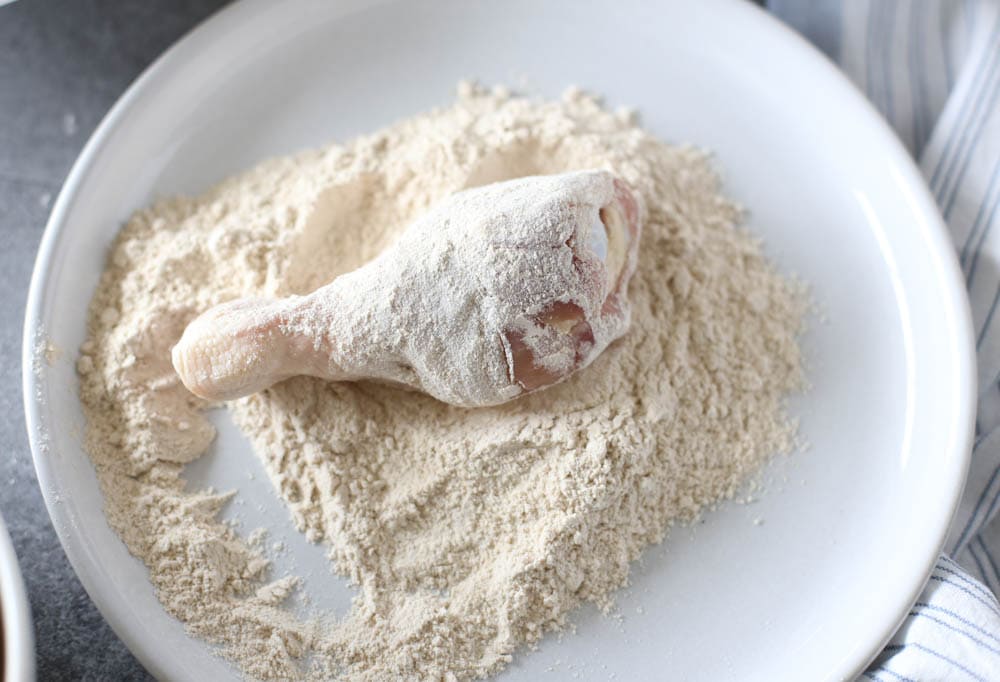 Chicken drumstick being rolled in flour.