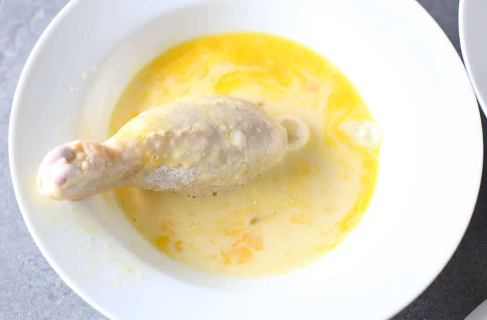 Floured chicken drumstick being rolled in egg and milk.