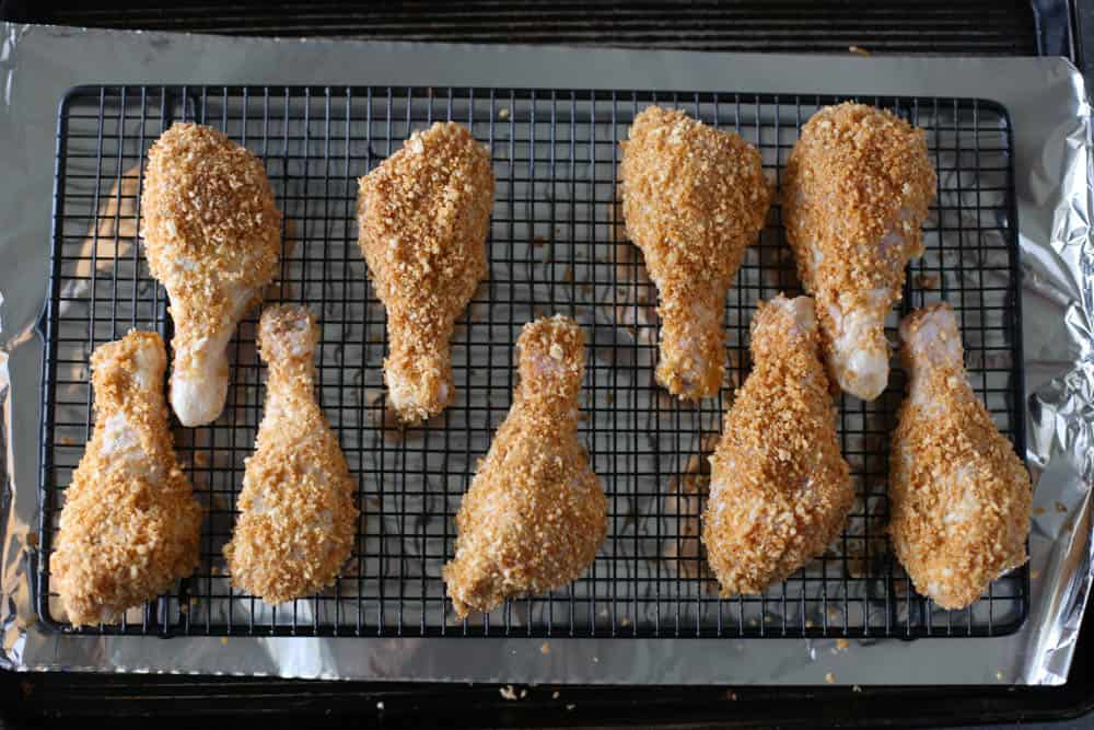 Breaded drumsticks on a baking rack on a foil-lined baking sheet.