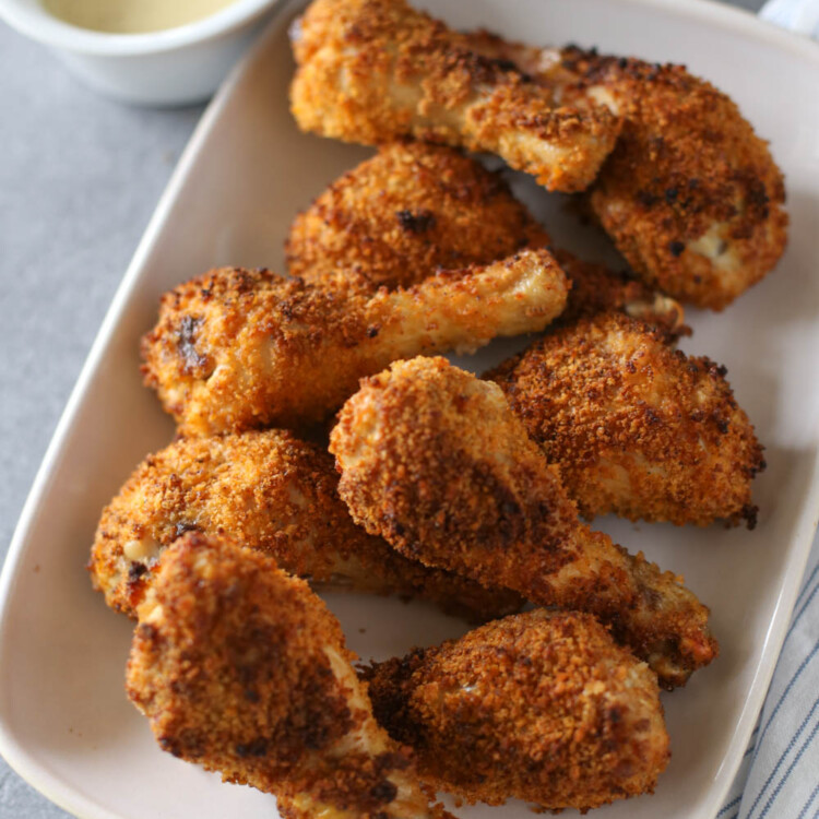 Crispy baked drumsticks served with honey mustard dipping sauce on a white platter.