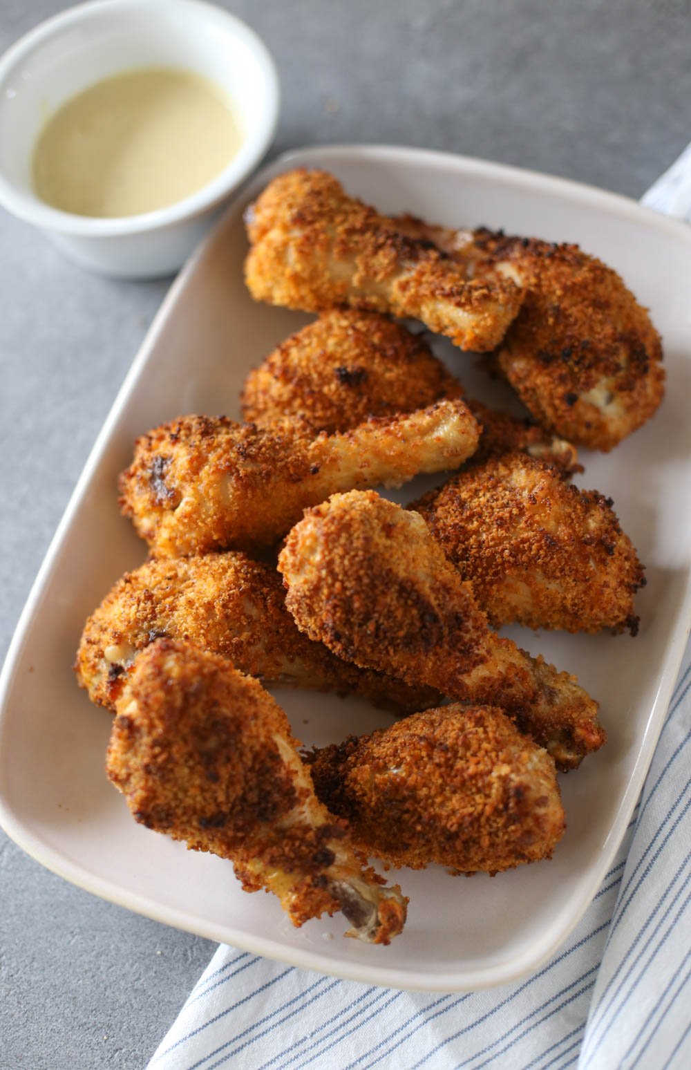 Crispy baked drumsticks served with honey mustard dipping sauce on a white platter.