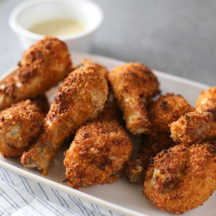 Crispy baked drumsticks on a platter with honey mustard dipping sauce next to it.