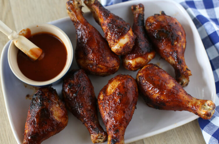 BBQ drumsticks on a white rectangle platter with a small bowl of BBQ sauce.