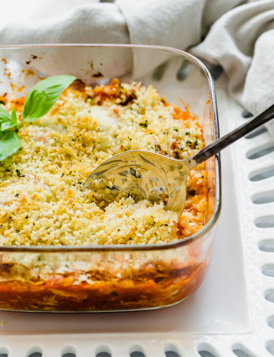 Chicken Parmesan casserole in a glass baking dish being served with a large spoon.