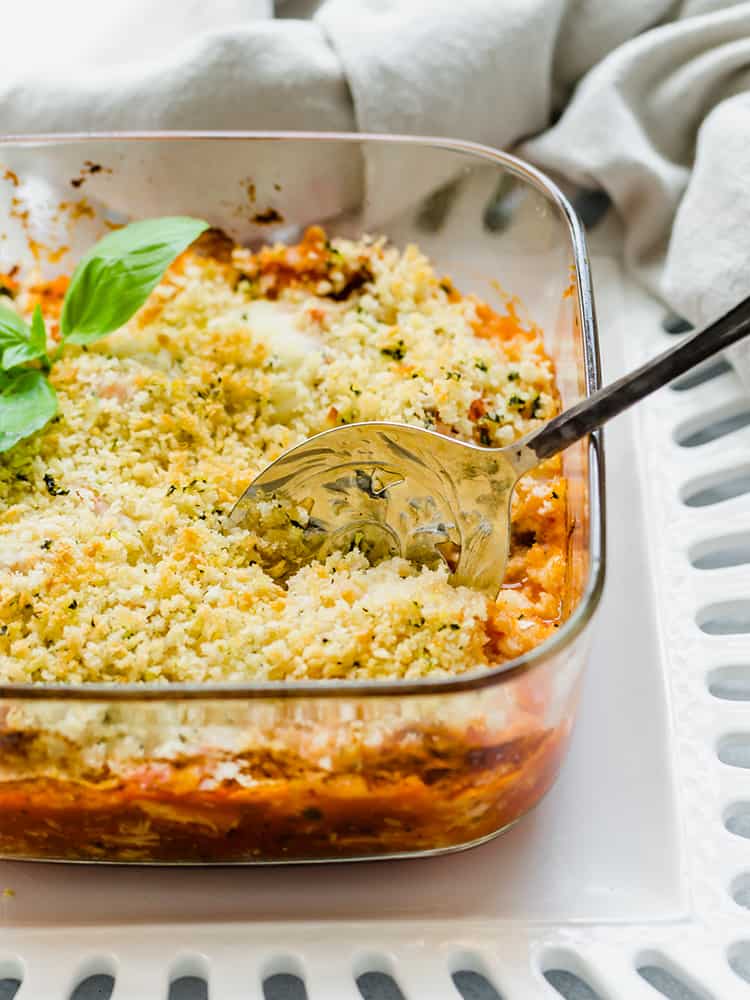 Chicken Parmesan casserole in a glass baking dish being served with a large spoon.