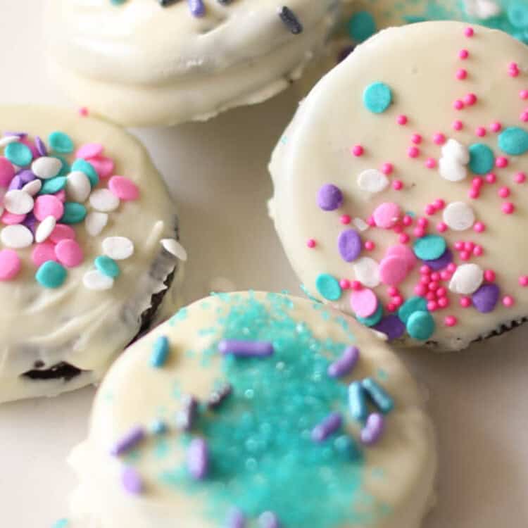 White chocolate covered Oreos with different color sprinkles on a plate.