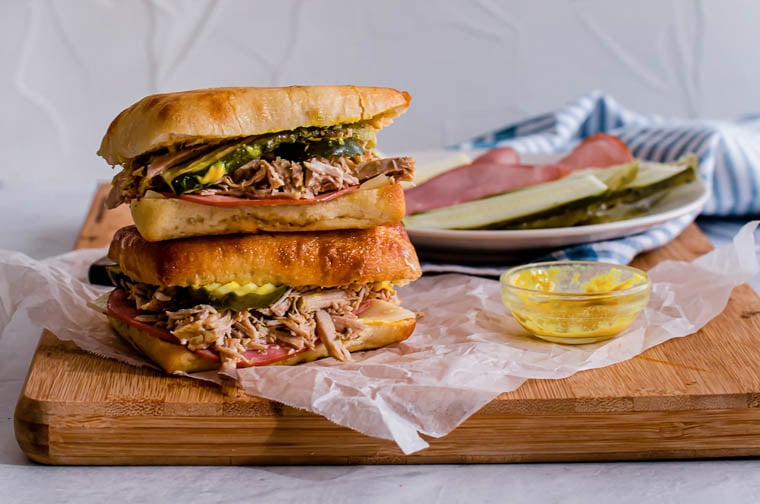 Two Cuban paninis stacked on top of each other with pickle slices on the side.