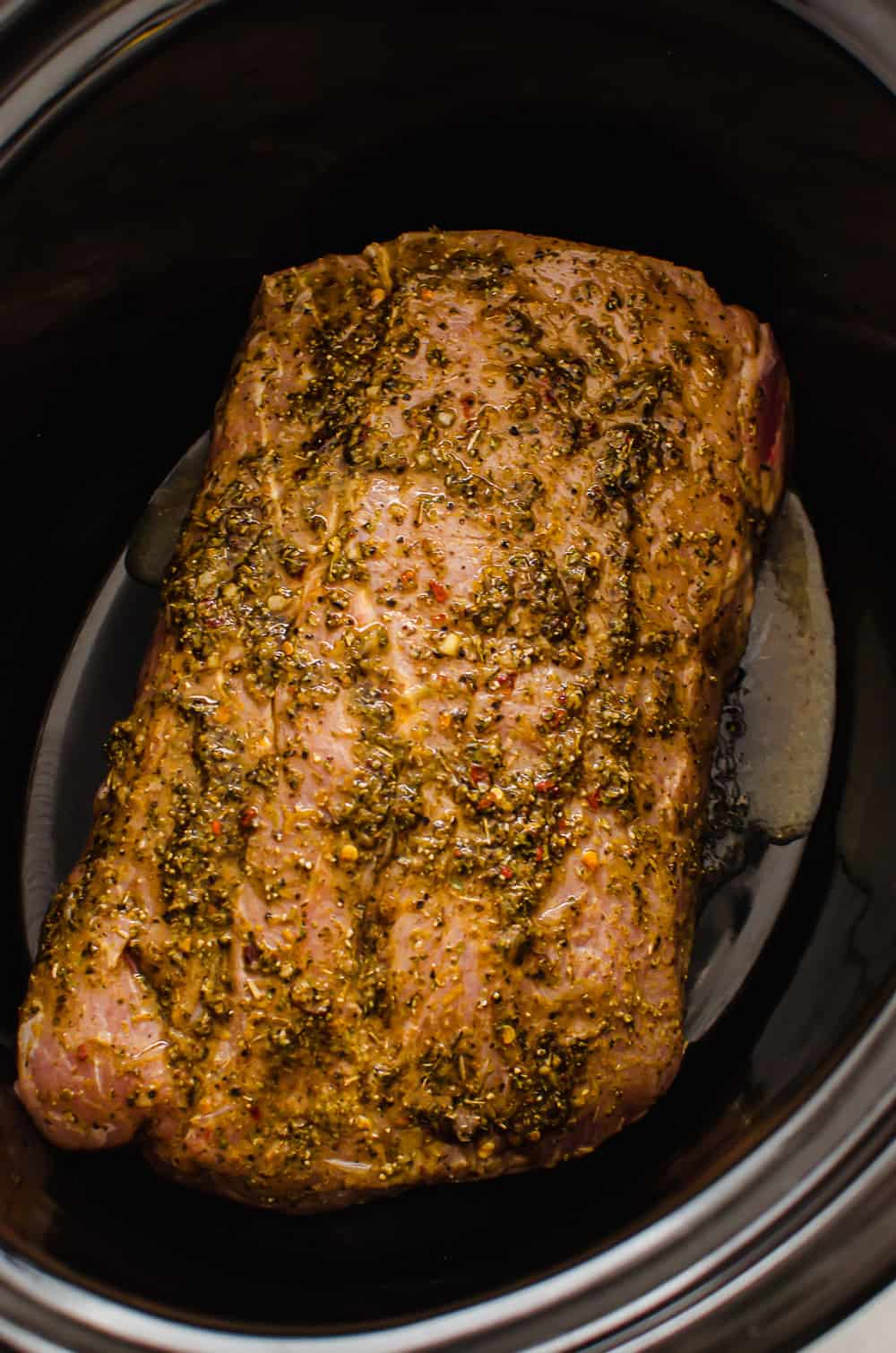 A pork shoulder smothered in seasonings in a slow cooker.