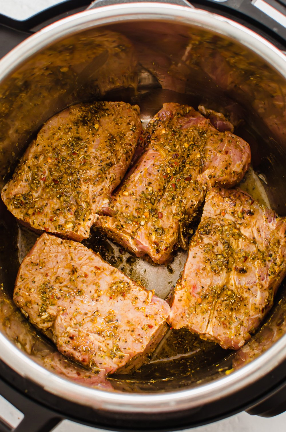A seasoned and quartered pork shoulder in an Instant Pot before cooking. 