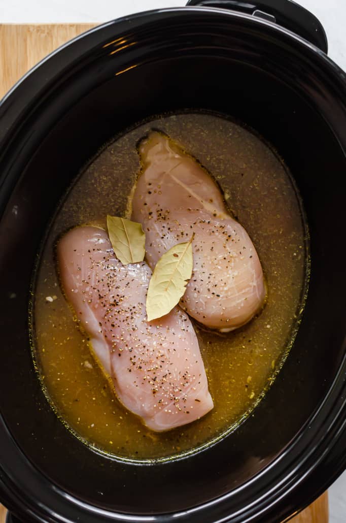 chicken broth, chicken breasts, seasoning, veggies, and bay leaves in a slow cooker