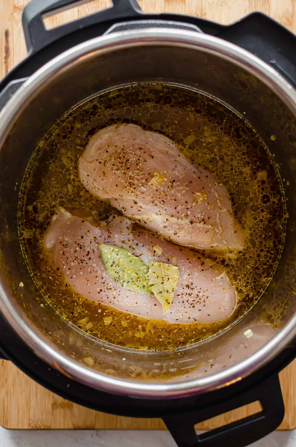 Two chicken breasts and some broth and bay leaves in the Instant Pot.