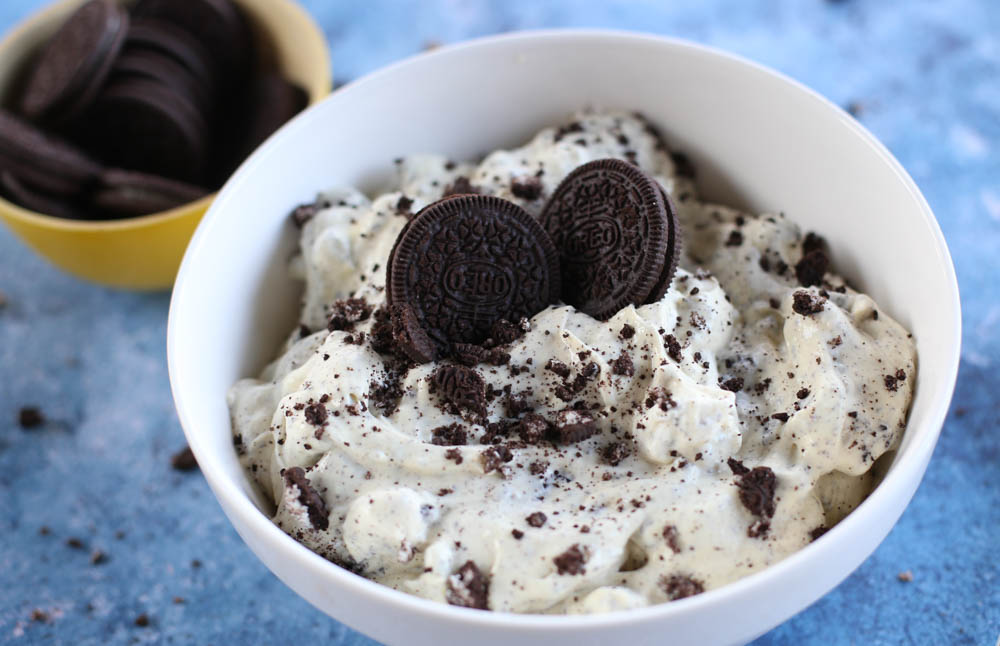 A serving of Oreo fluff in a white bowl with a small yellow bowl of Oreos in the background.