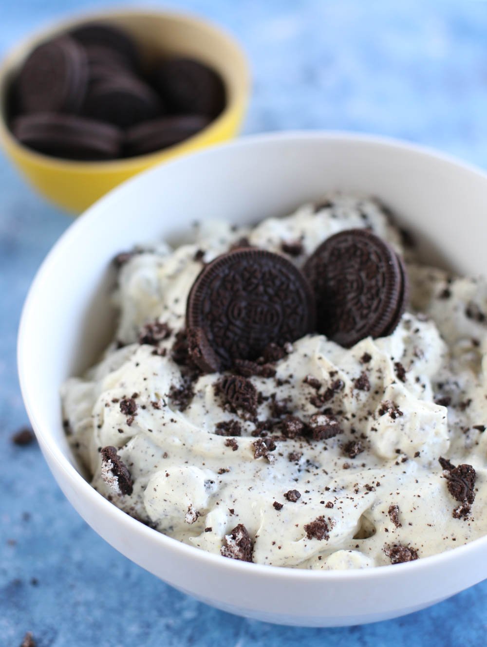 Oreo Fluff in a white bowl with two whole Oreos on top and a small yellow bowl with more Oreos in the background.