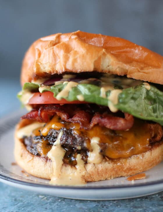 A smash burger with lettuce, tomato, bacon, and secret sauce on a plate.