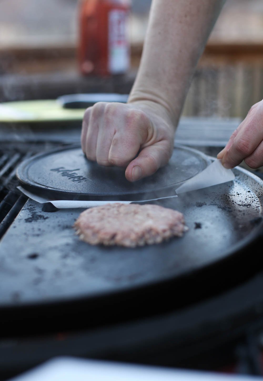 A hand pressing a burger press on top of a ground beef patty.