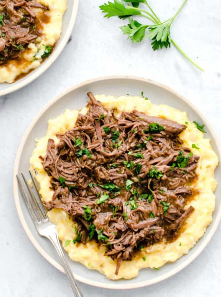 Balsamic shredded beef on a bed of polenta with chopped fresh parsley on top.