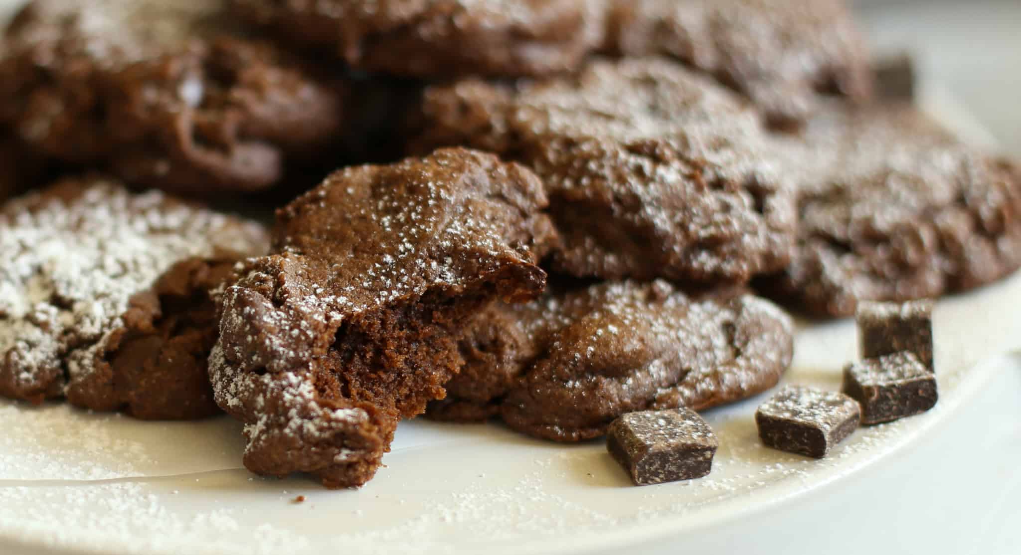 A dark chocolate coffee cookie broken in half sitting in front of a plate of cookies.