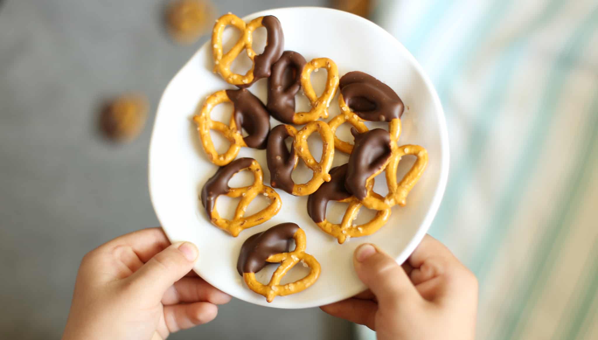 A child's hands holding a plate of peanut butter chocolate dipped pretzels.