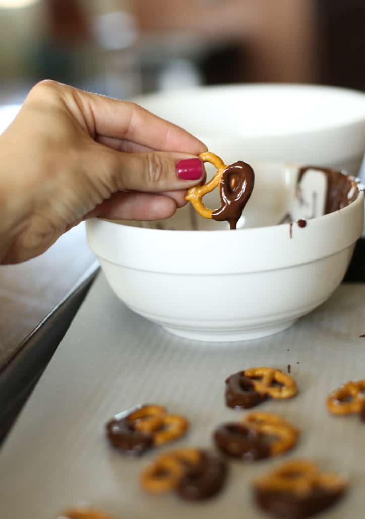 A hand dipping a pretzel into melted chocolate