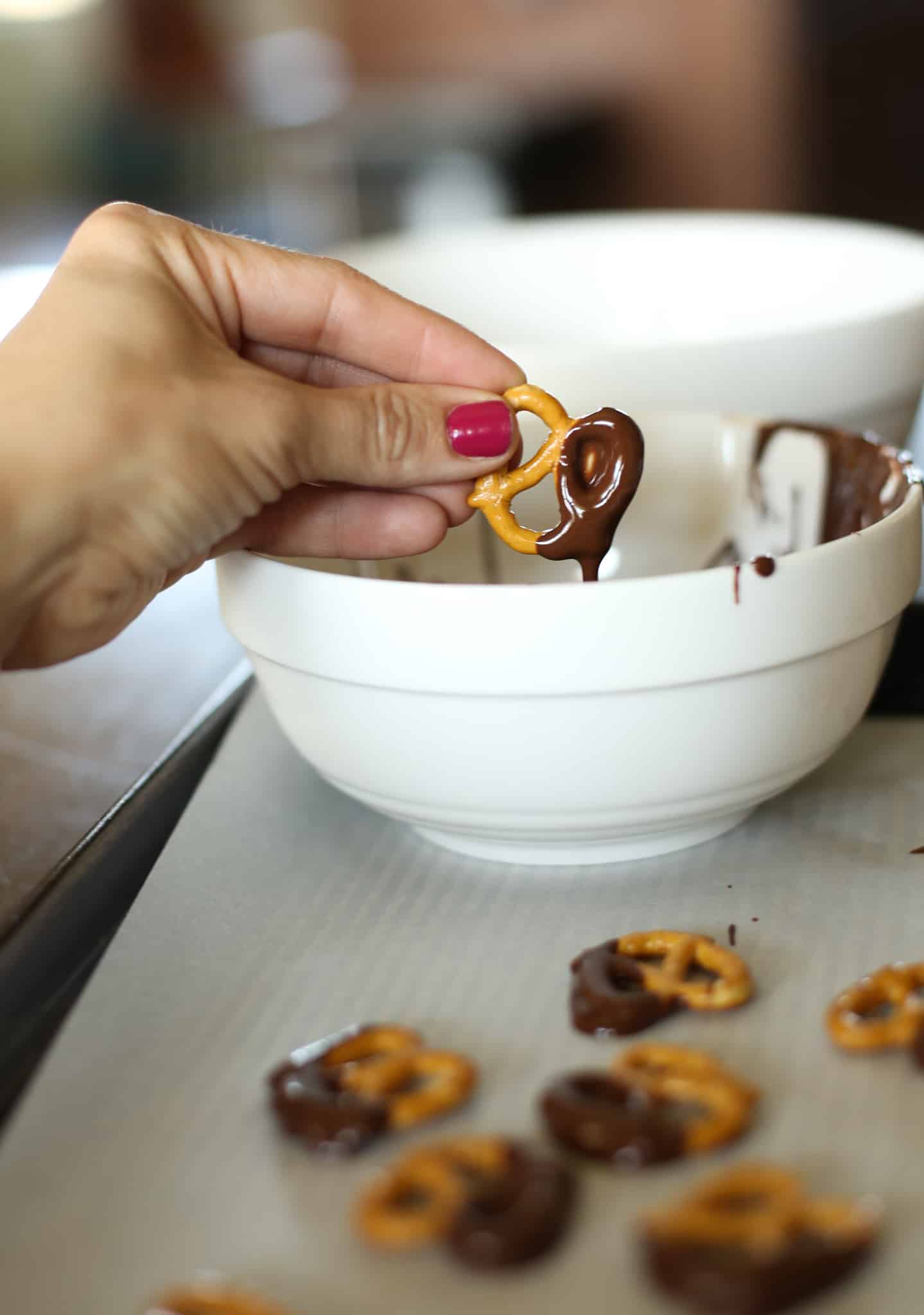 A hand dipping a pretzel into melted dark chocolate and peanut butter.