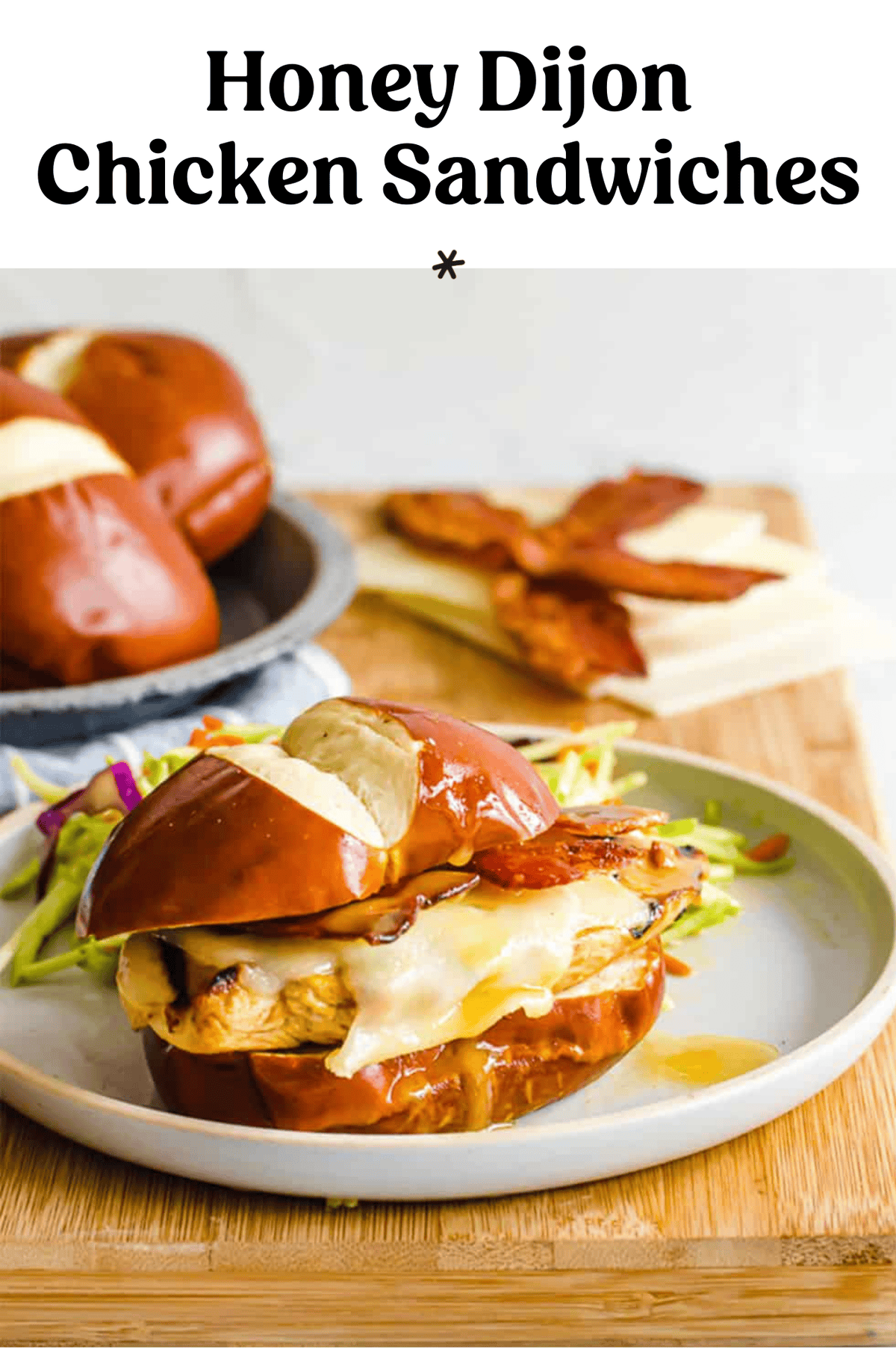 A honey Dijon chicken sandwich on a pretzel bun with swiss cheese and bacon on a plate.