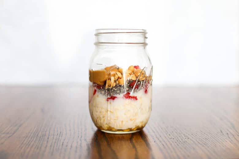 Peanut butter, chia seeds, chopped peanuts, and strawberry jam added to overnight oats in a mason jar. 