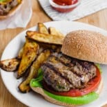Grilled burger on a bun with oven fries on the side.