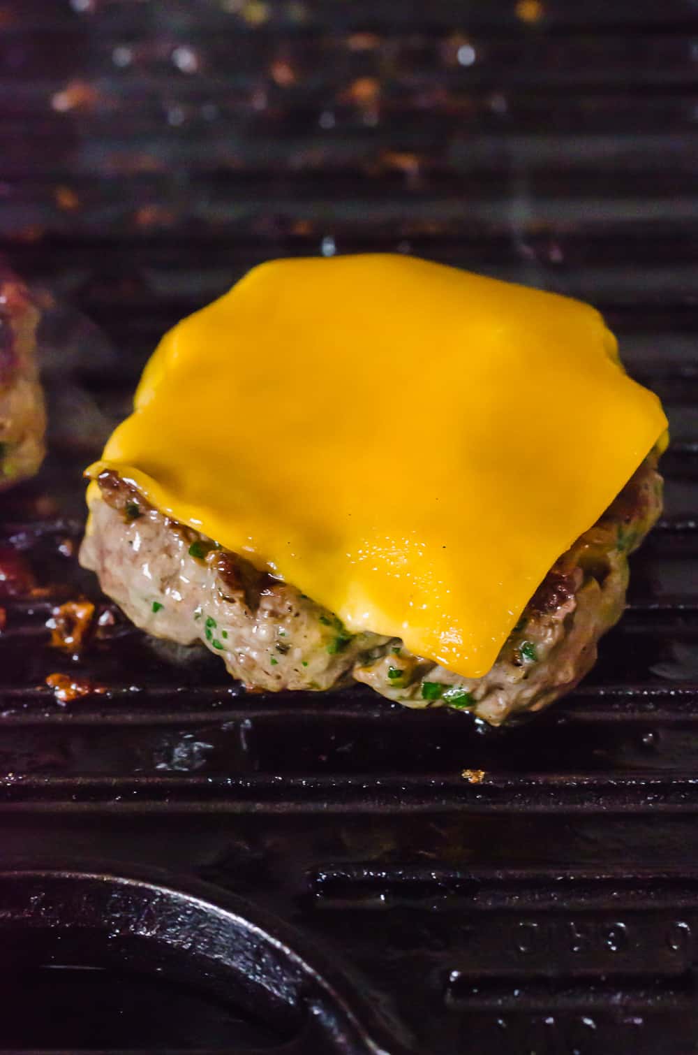 Burger on a grill with a slice of cheddar cheese melting on top.