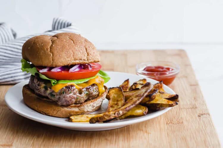 Cheesy chive burger on a plate with oven steak fries.