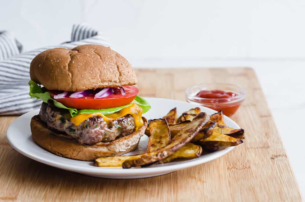 Cheesy chive burger on a whole wheat bun with lettuce, onion, and tomato and oven fries on the side.