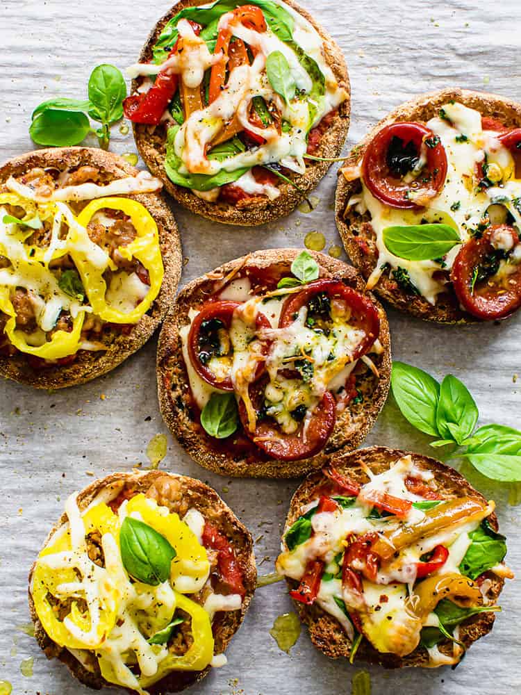 English muffin pizzas lined up on parchment paper.