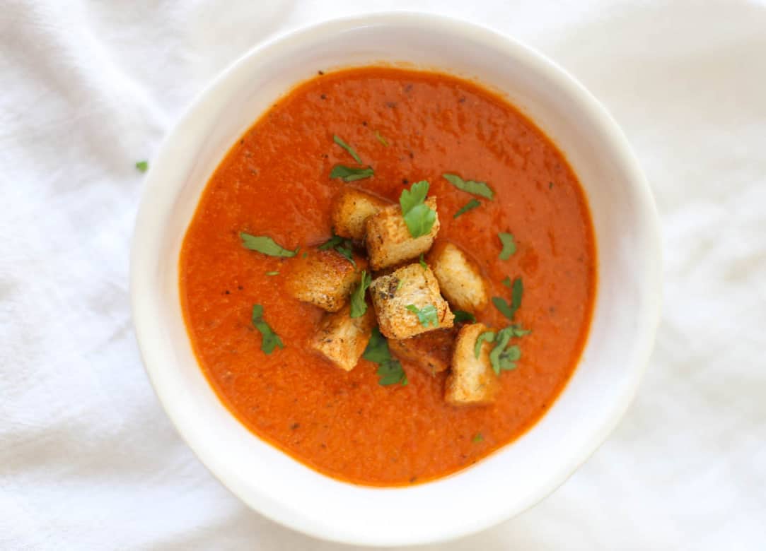 Instant Pot tomato soup in a white bowl with croutons on top.