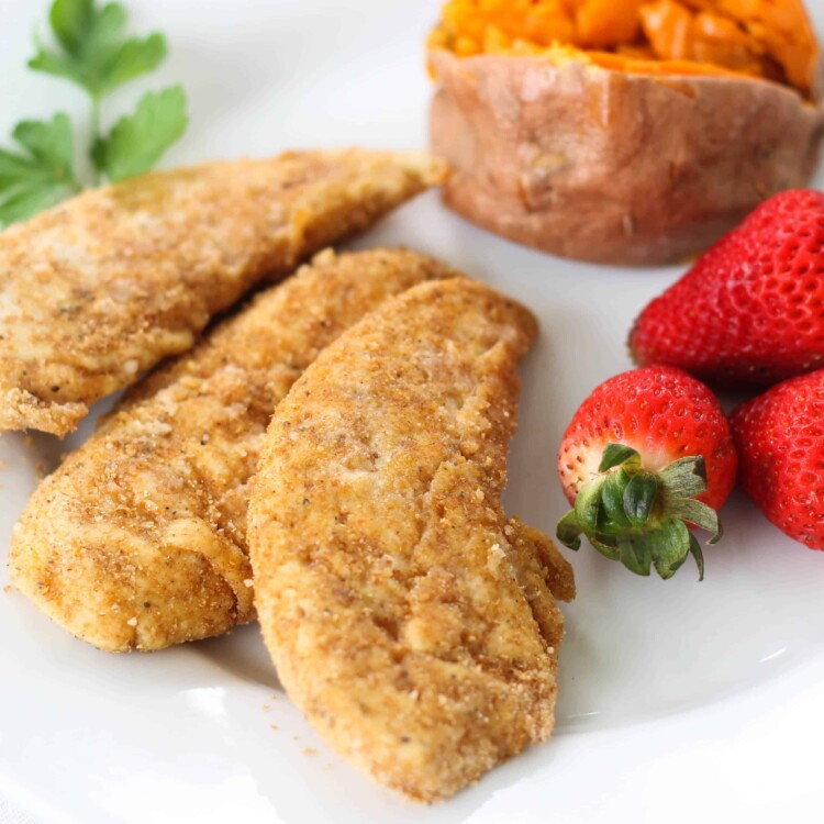 Three chicken tenders on a plate with strawberries and a baked sweet potato.