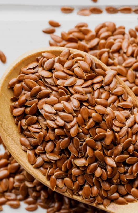 Whole flaxseed on a wooden spoon with more in the background.