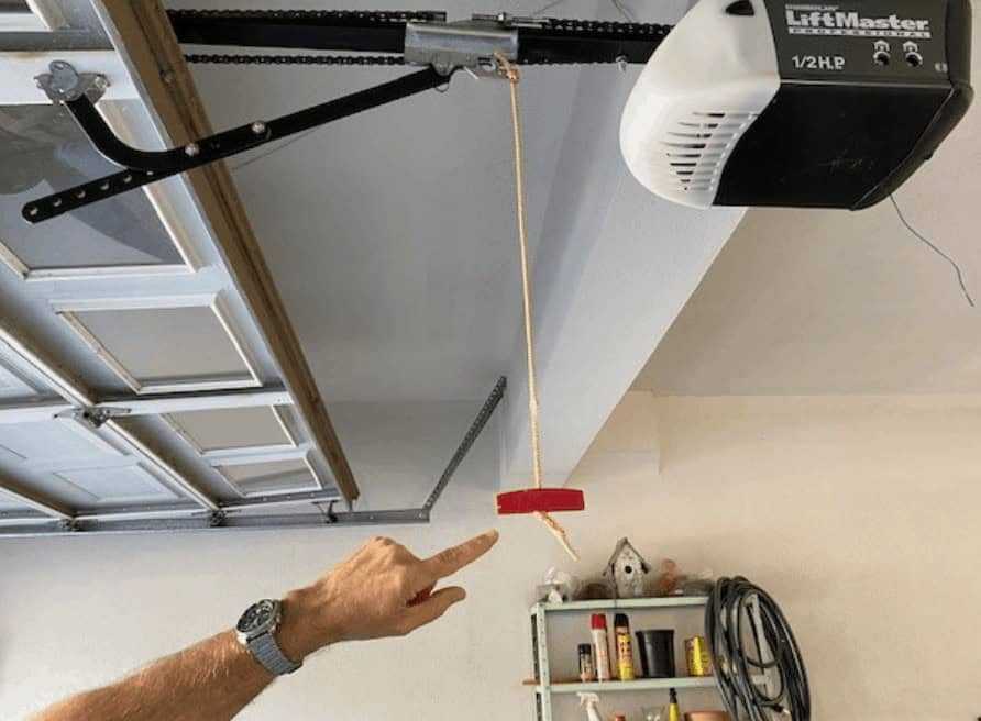 A hand pointing to the emergency release handle in a garage.